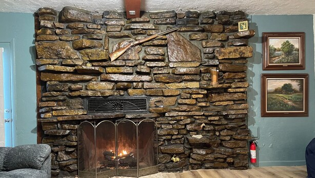 Una chimenea de piedra con fuego, un repisa de madera y dos cuadros en la pared.