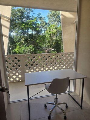 A balcony with a white table and chair, a lattice partition, and a view of trees and a rocky area. - Penthouse Studio in the Jungle - Relax & Nature (Tulum)