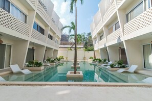 A pool area with lounge chairs and potted plants, surrounded by multi-story buildings with balconies. - Penthouse Studio in the Jungle - Relax & Nature (Tulum)