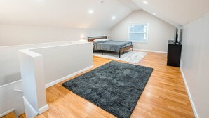 Ein Schlafzimmer mit einem Bett, einem Fenster, einem schwarzen Lautsprecher und einem grauen Teppich.