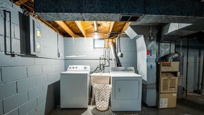 Ein Waschraum mit zwei Waschmaschinen, einem Trockner und einem Hauswirtschaftsraum mit Warmwasserbereiter und Lüftungsanlage.