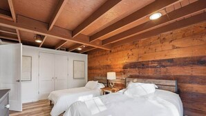 Un dormitorio con dos camas, paredes de madera, un armario blanco y una mesita de noche con una lámpara.