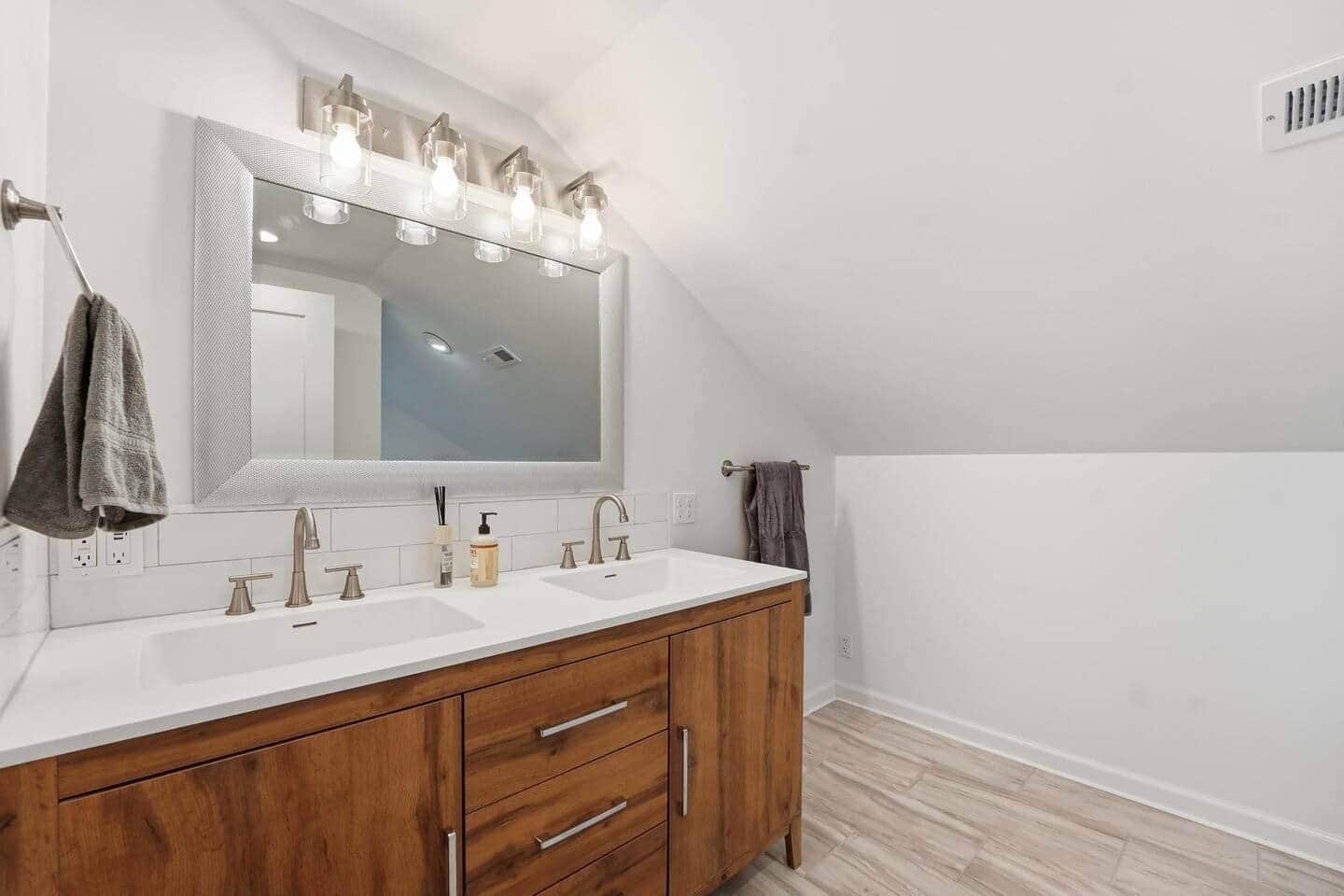 Une salle de bain moderne avec un grand miroir, deux lavabos, un meuble-lavabo en bois et un porte-serviettes.