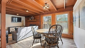Interior acogedor de una cabaña con una mesa de comedor, sillas, un sofá y un televisor montado en la pared.