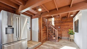 Una cocina con refrigerador de acero inoxidable, piso de madera y una escalera que sube a otro nivel.