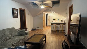 A living room with a sofa, coffee table, and a ceiling fan. There is a kitchen area with a refrigerator, microwave, and stools. - 2-bedroom studio sunny bright north hill location. (Pendleton)