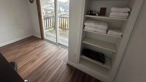 A room with a wooden floor, a sliding glass door leading to a balcony, and a built-in white shelving unit with folded towels. - 2-bedroom studio sunny bright north hill location. (Pendleton)