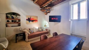 Een gezellige woonkamer met een houten plafond, een bank, een eettafel en een aan de muur bevestigde televisie.