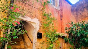 Un edificio rústico con una escalera de piedra que lleva a un arco, rodeado de follaje y plantas en macetas.