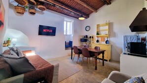Een knus woongedeelte met een eettafel, stoelen, een televisie waarop 'NETFLIX' wordt weergegeven, en een keuken met planken en een fornuis.
