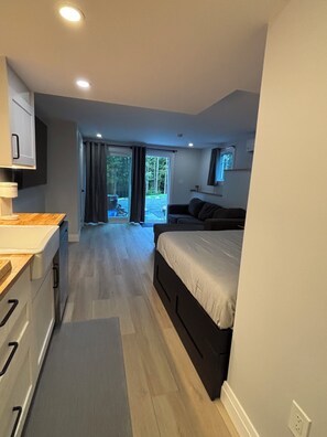A modern bedroom with a bed, a desk, and a view of a forested area through the window. - Cozy Meadowbroo studio - Trails & beaches close by! (Conquerall Bank)