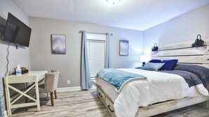 Un dormitorio con cama, escritorio, silla, televisor y ventana con cortinas.