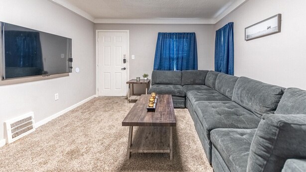 A living room with a sectional sofa, a coffee table, a TV, and a door. - Comfortable 3-Bedroom Home in a Great Central Location (Lincoln Park)