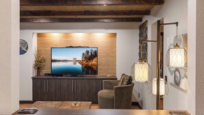 Un saló modern amb un televisor de pantalla plana fixat a una paret de fusta, un moble de fusta fosca a la part inferior i una zona de seients amb un sofà i butaques.