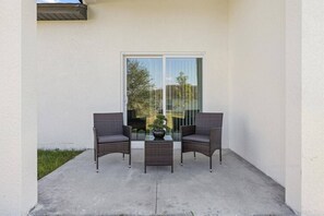 Un balcon avec deux fauteuils en osier et une petite table, une porte-fenêtre coulissante et un sol en béton.
