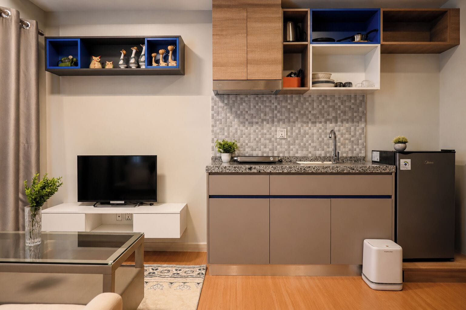 A modern kitchen with a flat-screen TV, a built-in oven, and a compact refrigerator.