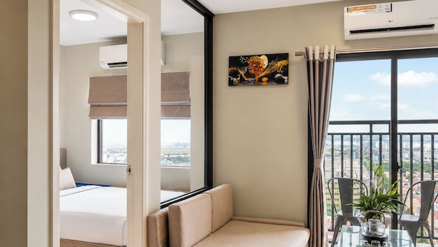 Habitación de hotel con cama, sofá, mesa de comedor con sillas, equipo de aire acondicionado y vista a la ciudad.