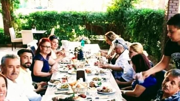 Un grupo de personas sentadas alrededor de una mesa larga al aire libre, disfrutando de una comida.