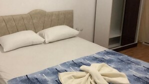Una cama con cabecera blanca, dos almohadas blancas y una manta azul con estampado de hojas.