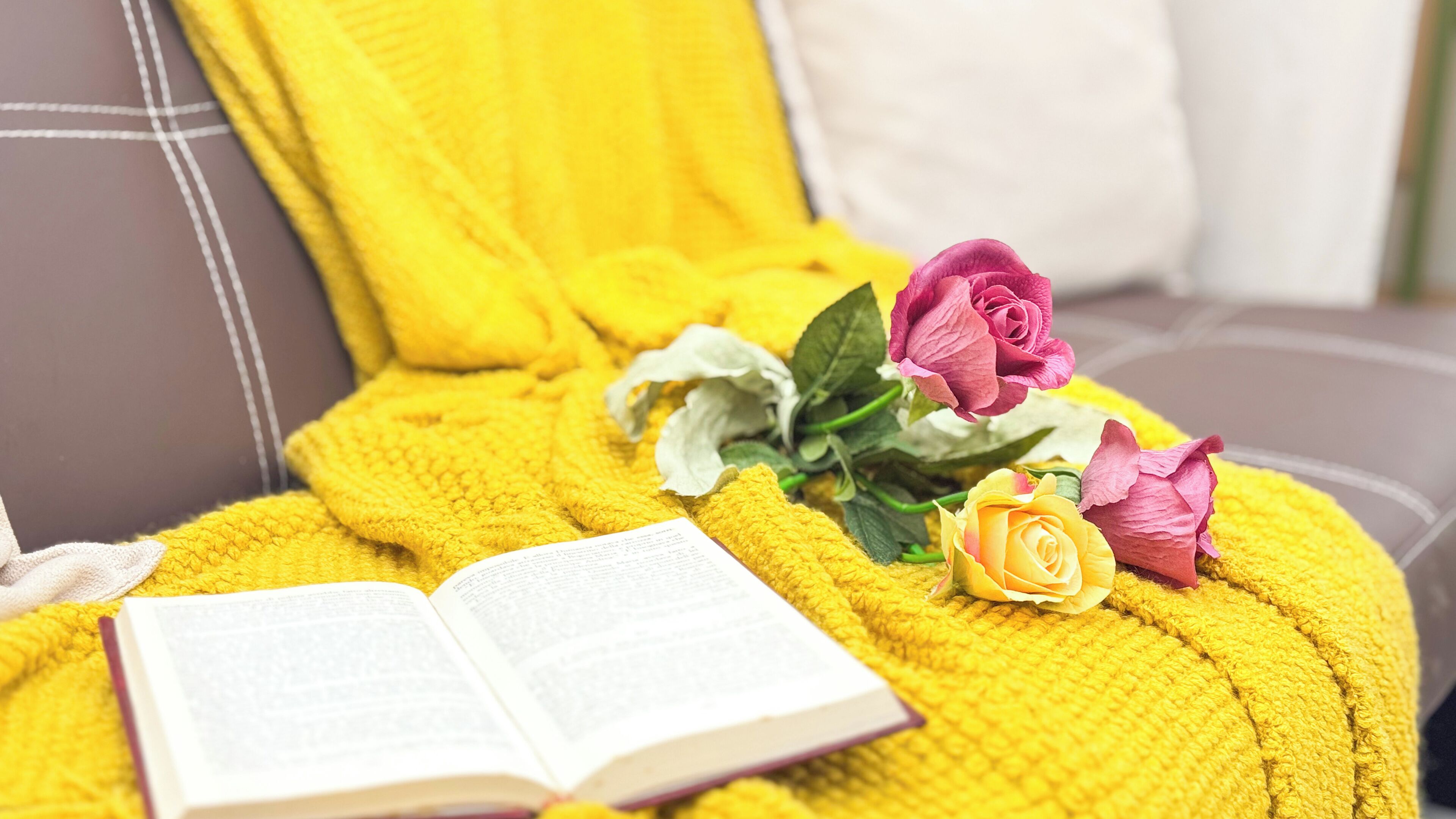 Un letto con una coperta gialla, un libro aperto e un bouquet di rose.