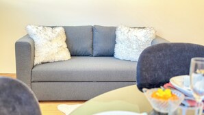 Ein graues Sofa mit flauschigen weißen Kissen, ein Holzboden und ein Glastisch mit Obst.
