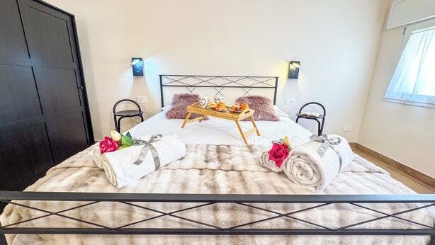 Ein ordentlich bezogenes Bett mit einer flauschigen Decke, ein Tablett mit Croissants und Kaffeetassen sowie zwei gerollte Handtücher mit Rosenblüten.