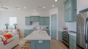 Una cocina moderna con armarios azul verdoso, encimera blanca y electrodomésticos de acero inoxidable.