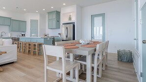 Una cocina moderna con armarios color turquesa, una isla central y un comedor con mesa y sillas blancas.