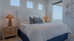 Un dormitorio con una cama, dos mesitas de noche, una lámpara auxiliar y vistas al mar.