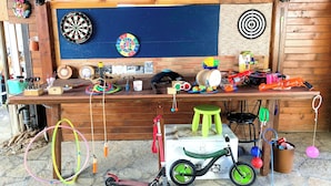 Een houten tafel met diverse kinderspeelgoed en spellen, waaronder hoepels, een scooter en een dartbord.