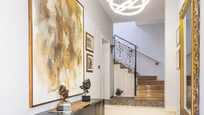 Un pasillo moderno con una consola de mármol negro, un cuadro abstracto de gran tamaño y una escalera con escalones de madera.