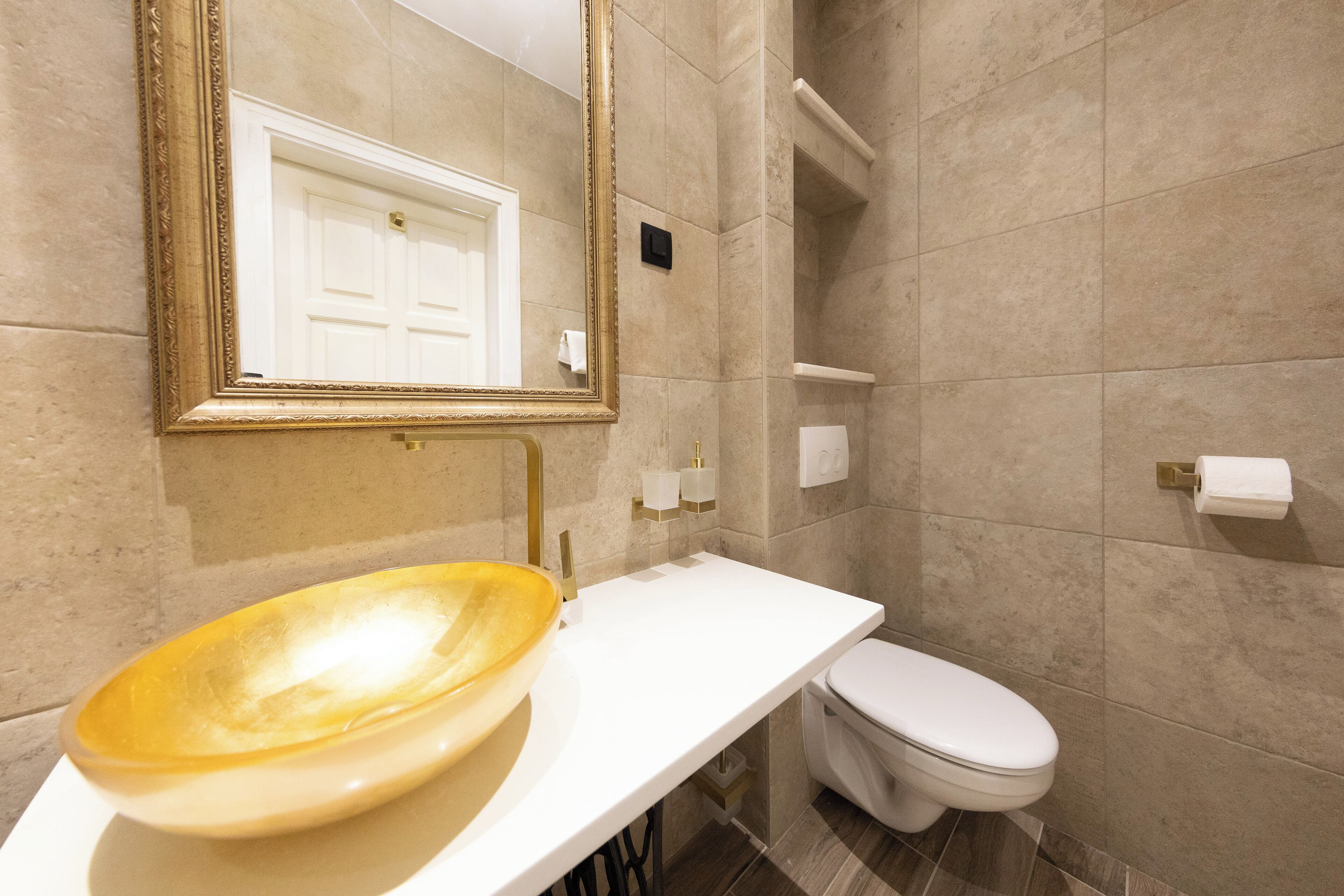 A bathroom with a large mirror, a white sink with a yellow bowl, a white toilet, and beige tiled walls.