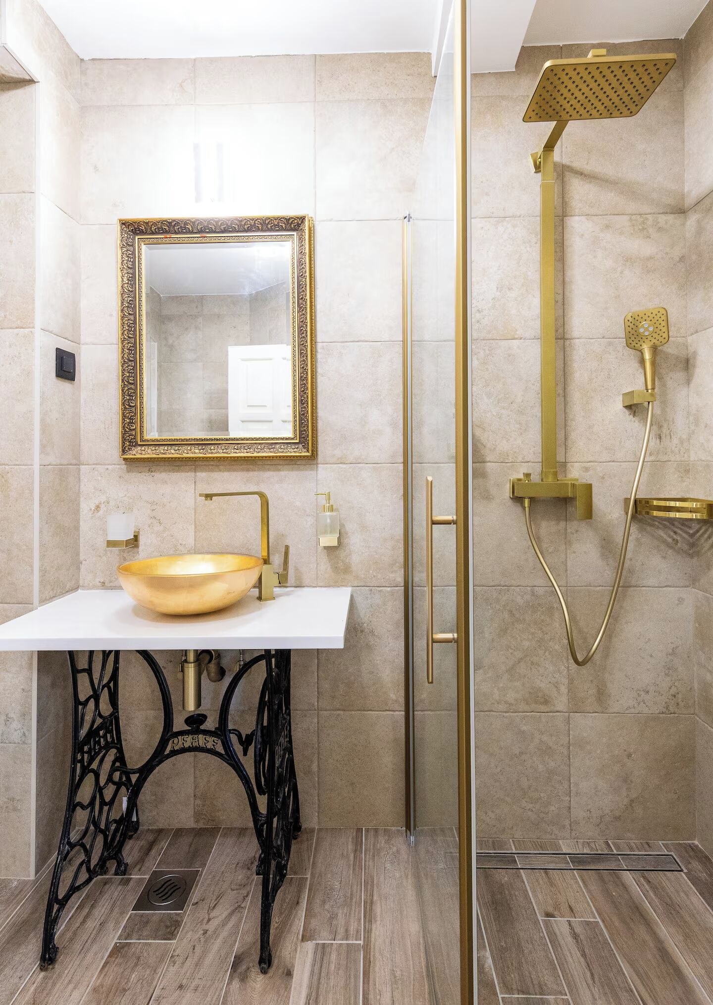 A bathroom with a white sink, gold fixtures, a large mirror, and a shower with a gold showerhead.