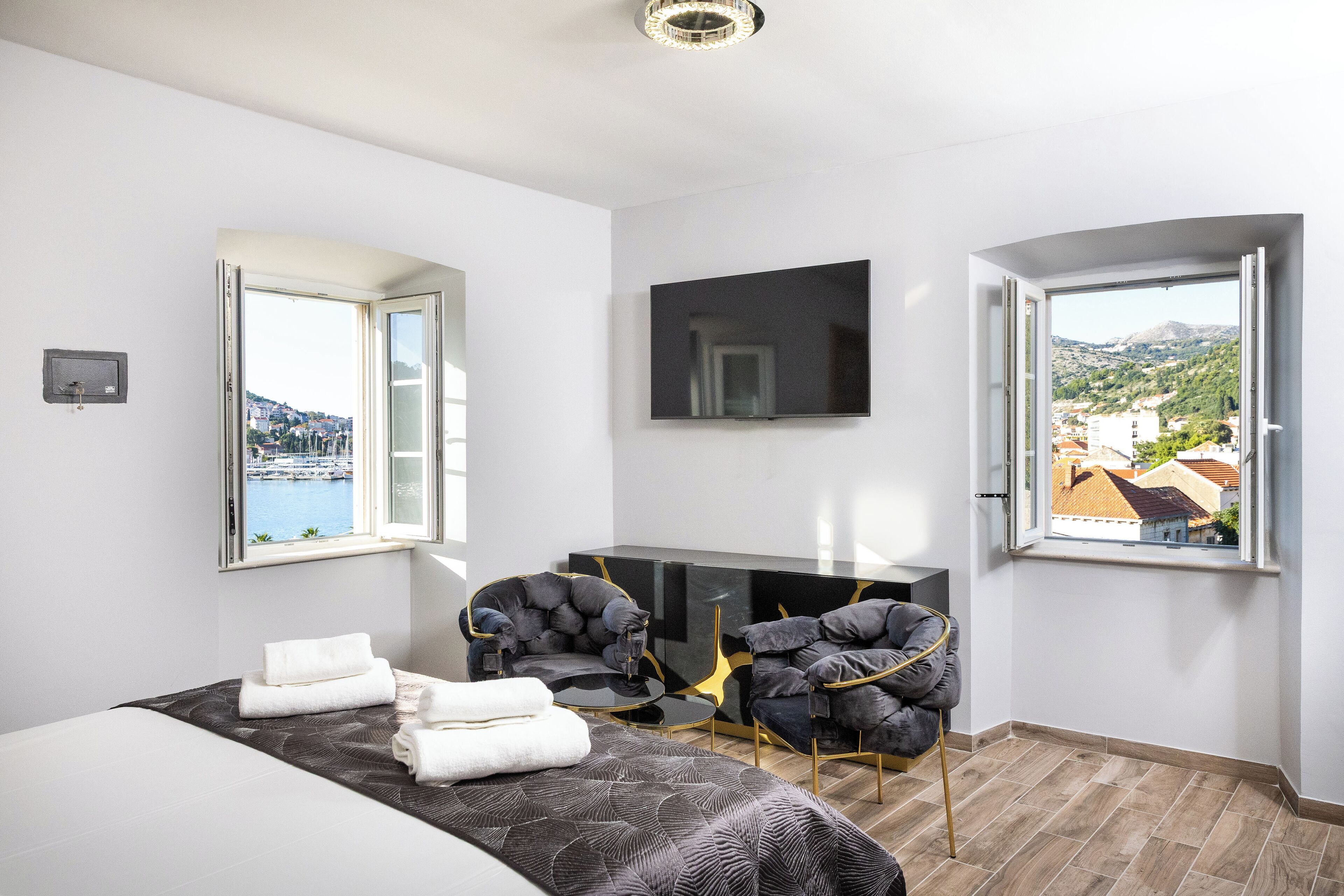 Camera d'hotel moderna con un letto, due poltrone, una TV e vista sul porto turistico e sulle colline.