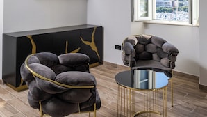 Un salón moderno con un televisor de pantalla plana montado en la pared, un mueble de entretenimiento negro y una zona de estar cómoda con una mesa redonda de cristal y sillones acolchados.