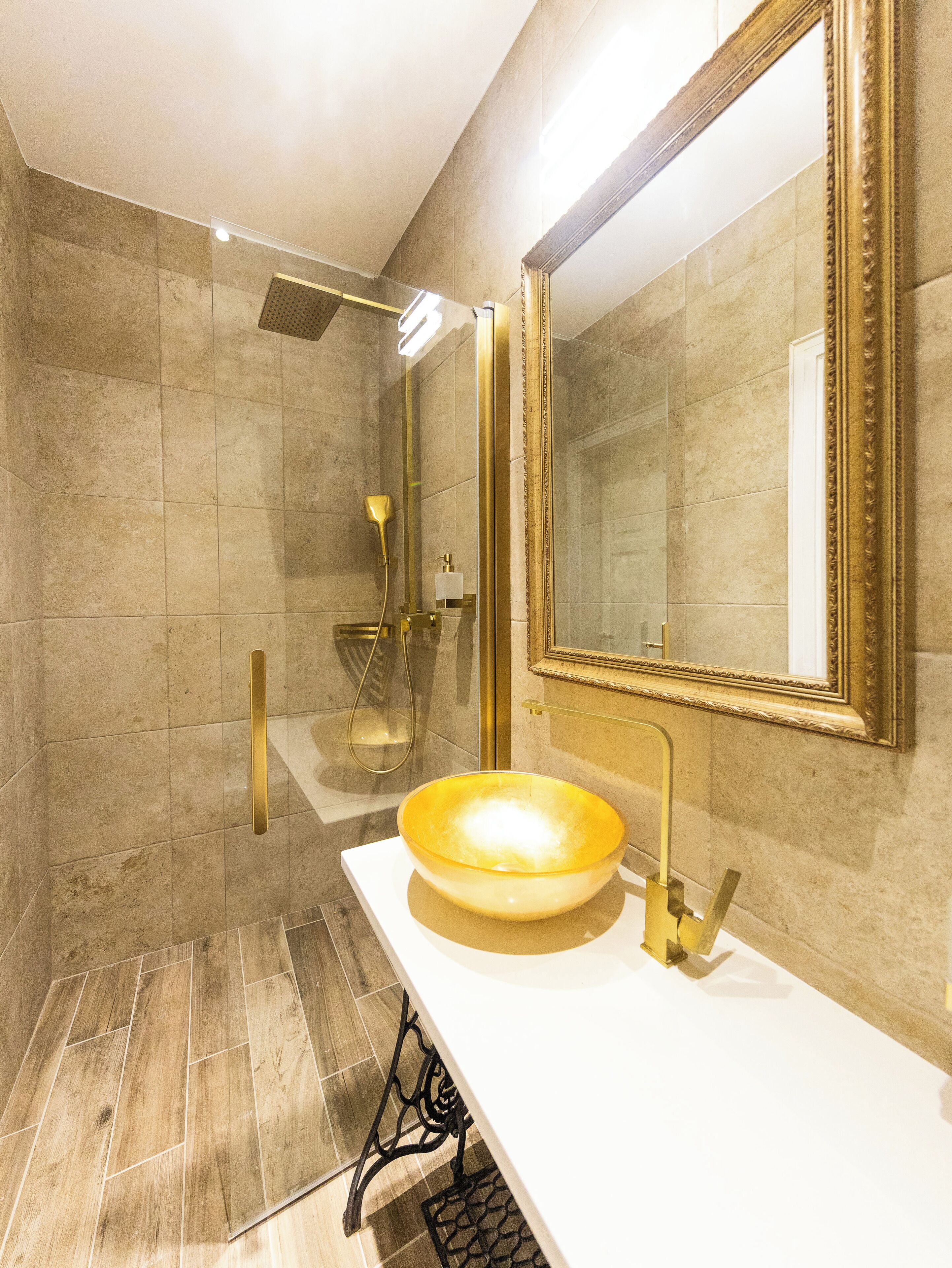 A modern bathroom with a large mirror, a gold sink, and a shower area.