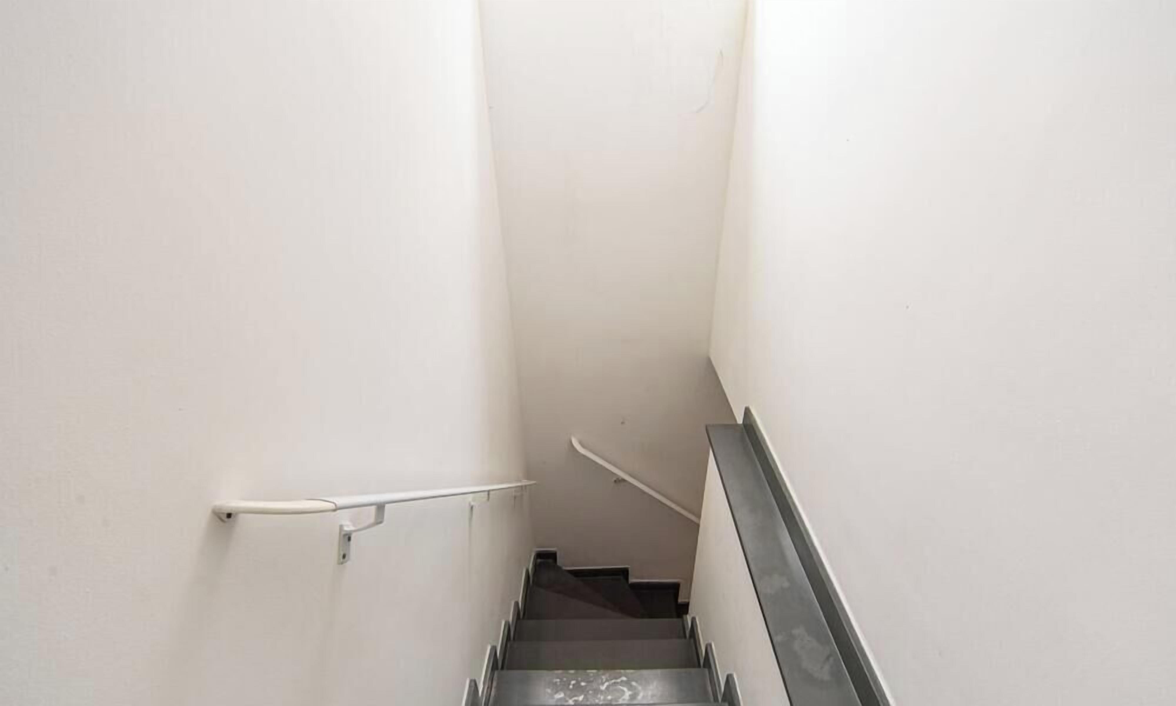 Een smalle trap met een leuning aan één kant en een metalen balustrade aan de andere kant.