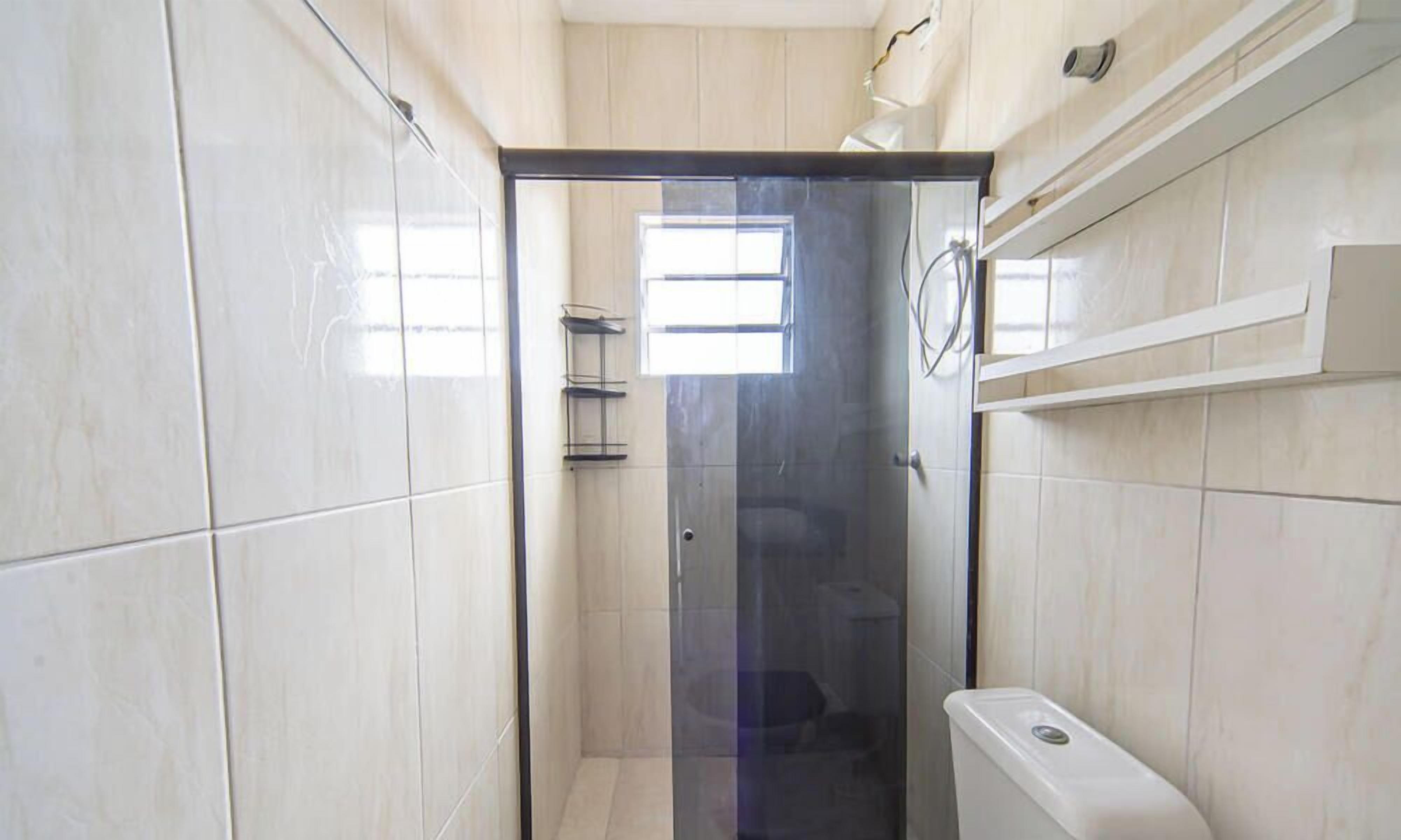Une salle de bain moderne avec une douche à l’italienne en verre, des murs recouverts de carreaux blancs et une fenêtre qui laisse entrer la lumière naturelle.