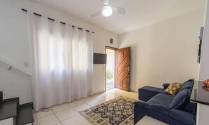 Ein Wohnzimmer mit einer Couch, einem Teppich mit Muster, einem Deckenventilator und einer Tür zu einem anderen Raum.