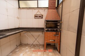 A kitchen with a brick oven, a drying rack, and a sign reading "Cantinho do Churrasco". - Casa em Mongaguá a 450m da Praia com Churrasqueira (Mongaguá)