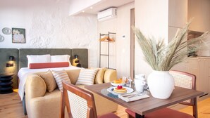 Una habitación de hotel moderna con una cama, una mesa de comedor con desayuno y un jarrón decorativo.