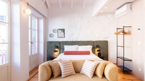 Un dormitorio con cama, mesitas de noche, lámpara colgante, ventana y aire acondicionado instalado en la pared.