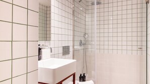 Ein modernes Badezimmer mit einer gläsernen Dusche, weißen Fliesen und einem weißen Waschbecken mit Spiegel darüber.