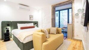Ein modernes Schlafzimmer mit Bett, Sofa, kleinem Tisch und Blick ins Freie.