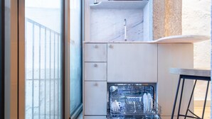 Eine kleine Küche mit integriertem Geschirrspüler, einer Marmorarbeitsplatte und einem Fenster mit Jalousien.