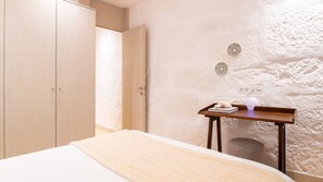 Ein Schlafzimmer mit einem Bett, einem Holzschrank, einem kleinen Tisch mit Lampe und einer strukturierten Wand.
