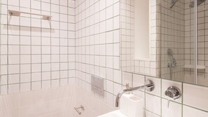 Ein modernes Badezimmer mit weißen, rechteckigen Fliesen, einer Duschkabine aus Glas, einem Handbrausekopf und einem Chrom-Waschbecken.