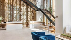 Un vestíbul modern amb taulell de recepció, seients blaus, una escala i un gran finestral.