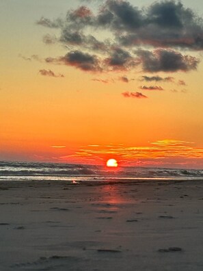 Een zonsondergang boven een strand, met golven en een heldere lucht.