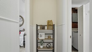 A hallway with a metal shelf unit displaying a sign, a potted plant, and decorative items. - Cozy 2BR / Close to Mayo Clinic / Full Kitchen & Private Backyard (Rochester)